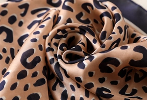 Close-up of leopard print silk scarf fabric with elegant satin sheen and folded texture