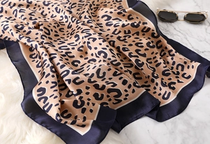 Detail of leopard print silk scarf with blue satin border on white marble background