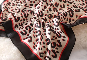 Macro shot of leopard print silk scarf showing glossy texture and elegant red borders