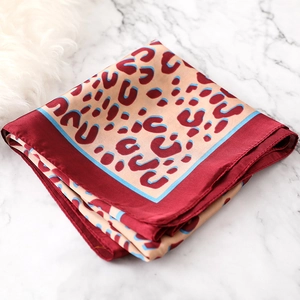 Detail of square leopard print silk scarf with red border on marble background