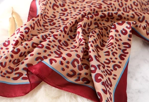 Detail of leopard print silk scarf with beige base and wine red edges on marble surface