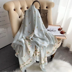 Floral silk-like scarf in light blue with wavy edges draped on an armchair