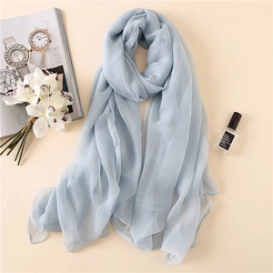 Hellblauer Chiffonschal mit Karomuster neben Blumen und Parfüm elegant präsentiert