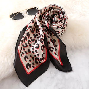 Leopard print silk scarf with red edges displayed on a white fur mat and marble table