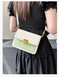 Detail of crossbody bag featuring green crocodile texture flap and gold buckle