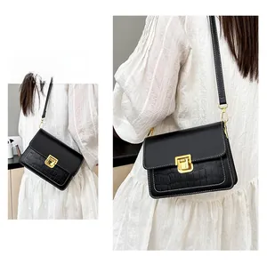 Detail of black crossbody bag with faux crocodile texture and gold magnetic buckle