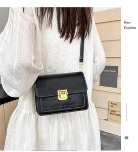 Detail of a vintage black crossbody bag with crocodile texture and golden metal lock clasp