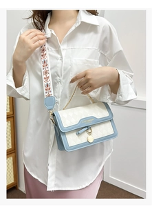 Detail of blue and white quilted crossbody bag with embroidered wide strap and metal chain