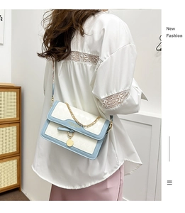 Detail of blue and white quilted crossbody bag with gold chain and circular pendant charm