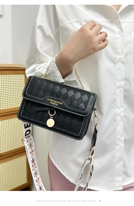 Detail of black quilted crossbody bag with wide printed strap and golden metal chain link