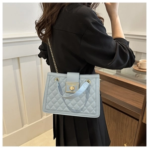 Detail of light blue quilted crossbody bag with gold metal lock and chain strap