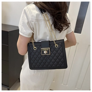Detail of black quilted leather shoulder bag with gold chain strap and square metal clasp