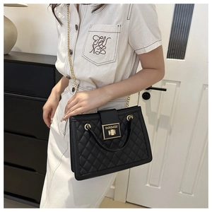 Close-up of black quilted chain bag with gold rectangular turn-lock and texture details