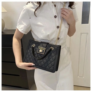 Detail of black quilted crossbody bag with gold chain strap and metallic clasp closure