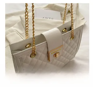 Detail of white quilted handbag showing golden chain strap and metallic twist lock