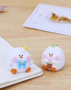 Detail of cute white duck figurines with a blue bow and pink flower pot on a wooden desk