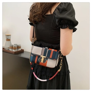 Detail of color-block plaid crossbody bag with gold metal lock on a black bubble sleeve dress