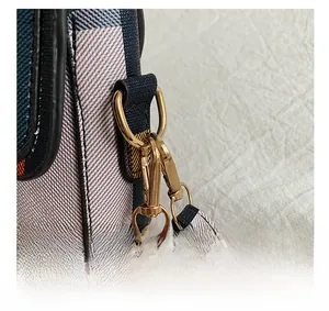 Detail showing the golden metal D-ring and swivel hook hardware on a plaid handbag