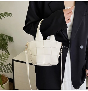 Gros plan du sac seau tressé crème avec détails dorés porté sur un blazer noir
