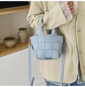 Détail du sac cabas tressé bleu clair avec boucles dorées sur une veste beige chic