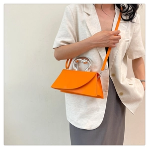 Detail of a bright orange mini handbag with a unique silver hollow metal handle