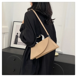 Detail of a beige geometric shoulder bag with a unique silver metal handle on a model