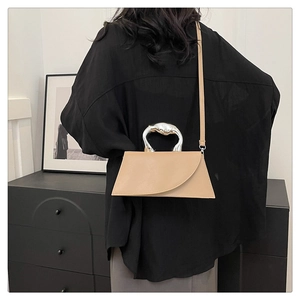 Detail of light khaki trapezoid bag featuring an ornate silver metal handle and leather texture