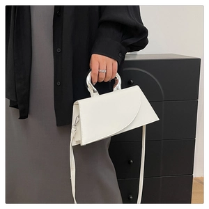 Close-up of white leather handbag featuring a unique semicircular silver metal handle