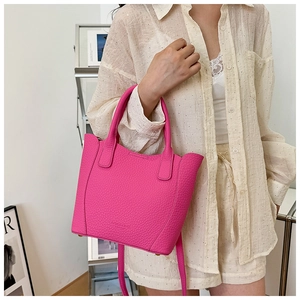 Détail du sac seau en cuir fuchsia à motif litchi avec poignées et bandoulière réglable