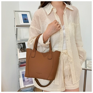 Détail d'un sac cabas en cuir marron à motif litchi avec poignées et bandoulière chic