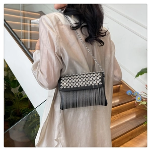 Detail of black crossbody bag featuring silver rhinestone studs and dangling chain tassels