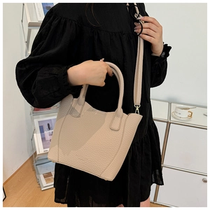 Gros plan du sac seau beige à texture lychee porté par un mannequin en intérieur
