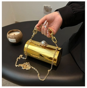 Detail der goldenen Zylinder-Clutch mit Perlenschnalle und Metallketten-Griffen