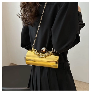 Detail einer goldenen zylindrischen Abendtasche mit Perlenverschluss und Kettenriemen