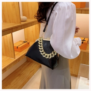 Detail of black shell bag featuring textured leather, gold chain, and metal frame clasp