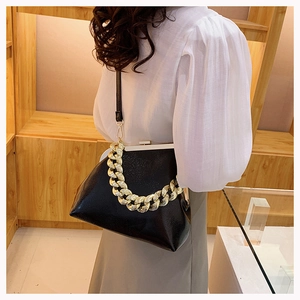 Detail shot of black textured leather bag with gold chunky chain and metal clasp closure