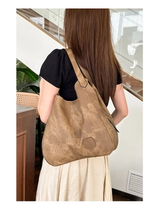 Close-up of vintage brown leather tote bag with embossed logo worn on the shoulder
