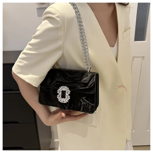 Detail of black glossy handbag with rhinestone buckle and silver chain on model