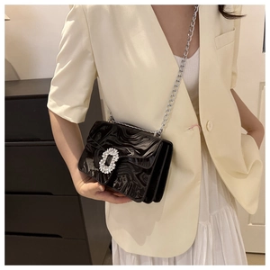 Close-up of black glossy crossbody bag featuring a large rhinestone buckle and chain
