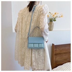 Detail of light blue crossbody bag with glitter texture and quilted pattern on model