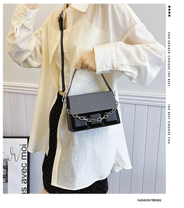 Detail of black box handbag featuring textured flap, silver chain and metal hardware