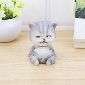 Linda figurita de gato gris a rayas con cabeza temblorosa en un escritorio de madera