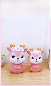 Detail view of two cute pink deer piggy banks with floral crowns on a wood surface