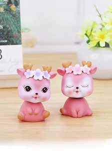 Close-up of pink deer bobblehead ornaments with flower headbands on a wooden desk