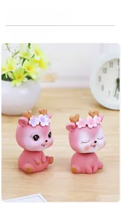 Detail of two cute pink resin deer car ornaments with floral antlers on wood background