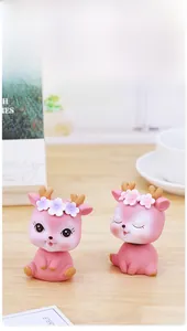 Macro shot of two pink resin deer sculptures with floral crowns on a wooden desk surface