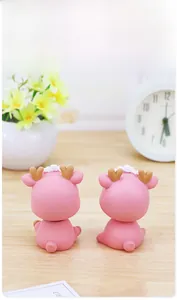 Rear view of two cute pink resin deer car ornaments on a light wooden table