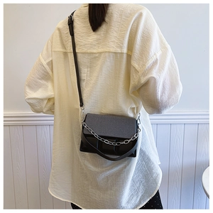 Detail of a chic black leather crossbody bag with a stylish silver metal chain handle