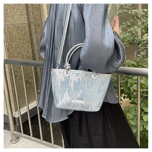 Detail of silver sequined bucket bag with knotted handles and metallic finish texture