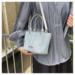 Detail of light blue textured tote bag with silver handles and knot design on the strap